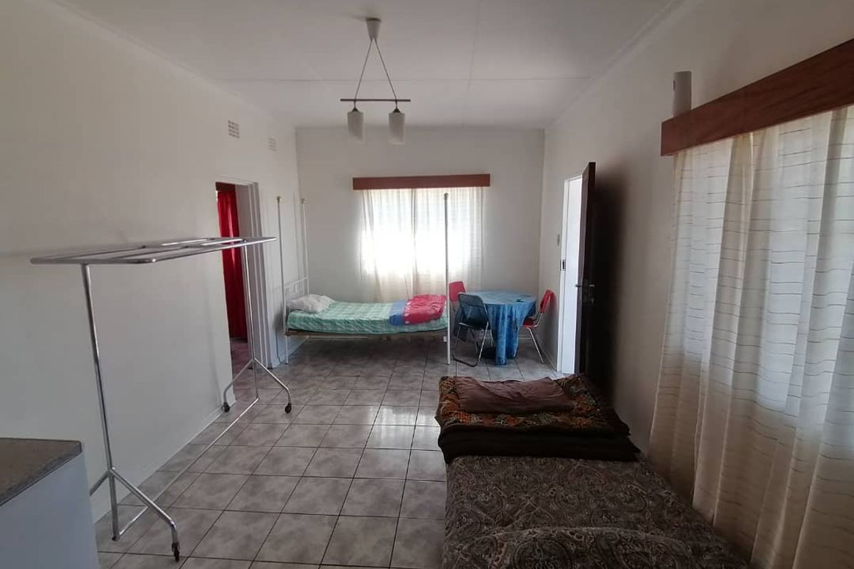 A functional bedroom space featuring tiled flooring, neutral walls, and natural light from windows with fitted curtain rods.