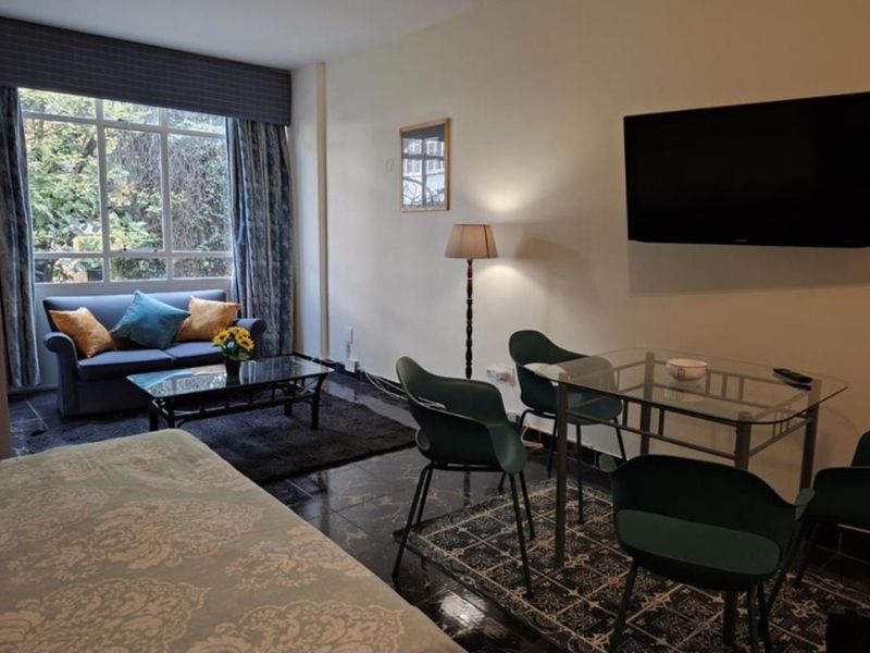 An open-plan living and dining area featuring dark tiled flooring, a large window with natural light, and a wall-mounted television.