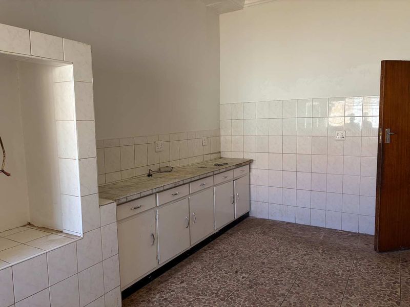 An empty kitchen featuring tiled countertops, built-in cabinetry, and tiled splashbacks, offering a blank canvas for renovation and modernization.