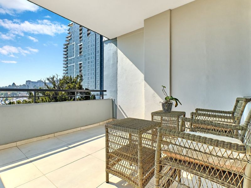A covered penthouse balcony featuring tiled flooring and a metal balustrade, offering an elevated urban view.