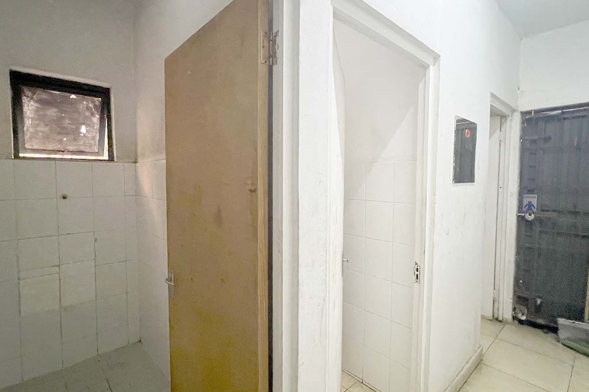 A functional bathroom area featuring tiled walls and flooring, with a shower fixture and a secure metal gate entrance.