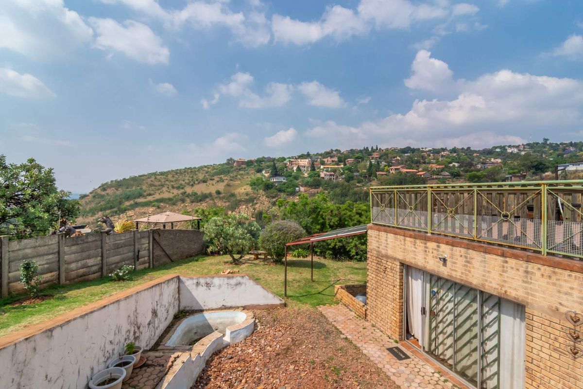 Rear exterior view featuring a brick house with an upper balcony, a small pool area, and a garden overlooking a scenic hillside landscape.