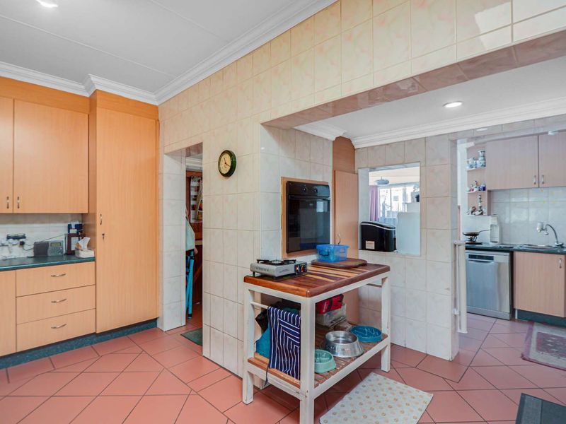 A functional kitchen featuring built-in cabinetry, tiled flooring, and a separate scullery area with integrated appliances and ample storage space.