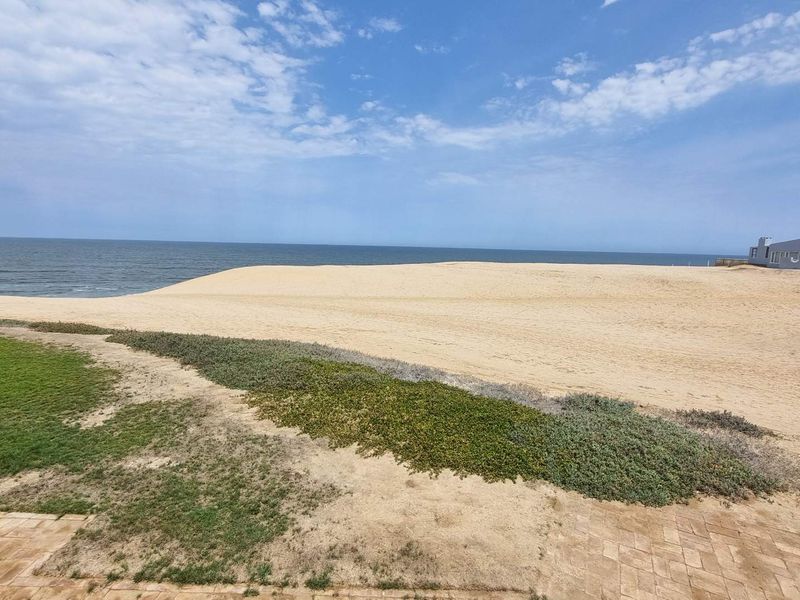 A scenic view overlooking the sandy beach and ocean, featuring a paved patio area in the foreground.