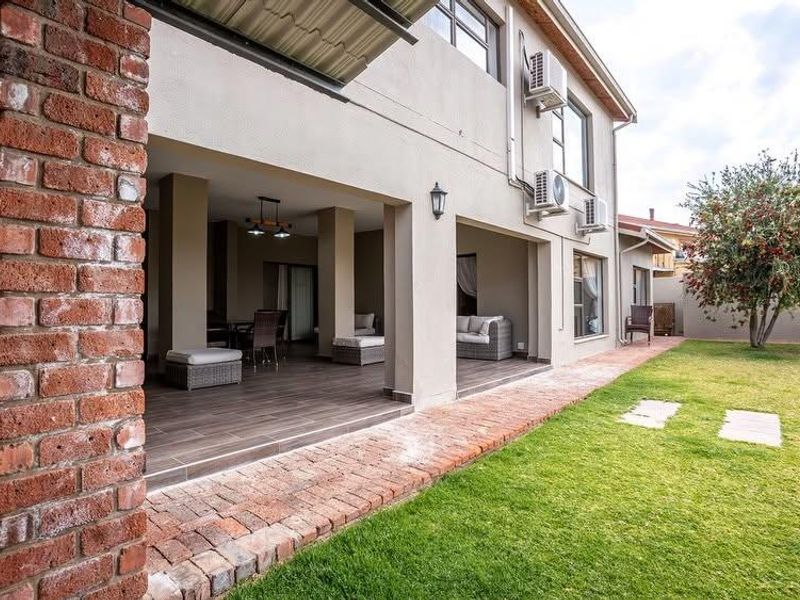Spacious covered patio featuring tiled flooring and exposed brick accents, overlooking a well-maintained garden area with integrated air conditioning units.