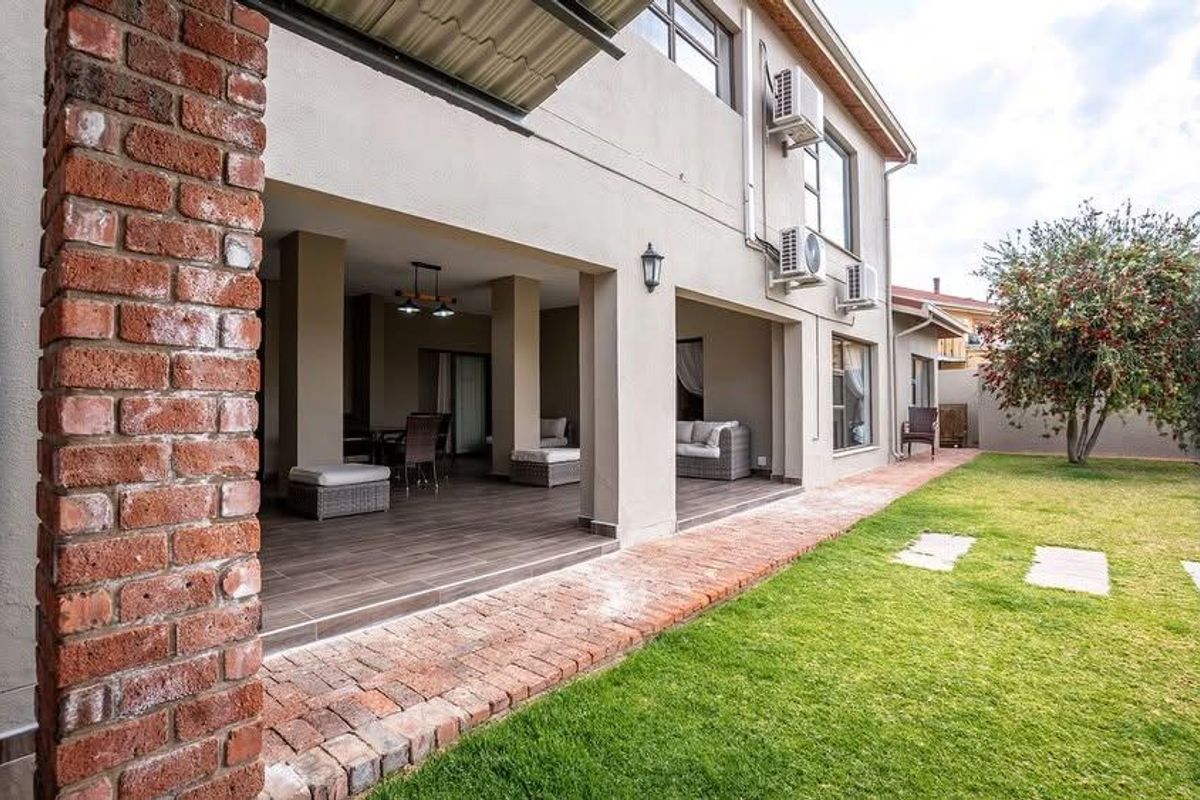 Spacious covered patio featuring tiled flooring and exposed brick accents, overlooking a well-maintained garden area with integrated air conditioning units.