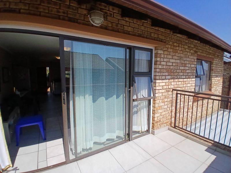 A tiled balcony area featuring a metal balustrade and sliding glass door access to the interior living space, set against a face brick exterior.