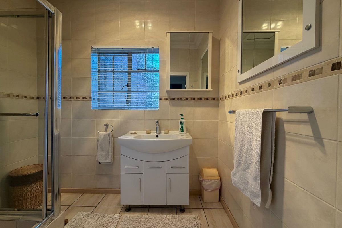 A functional bathroom featuring a vanity cabinet, shower enclosure, and neutral wall and floor tiling.