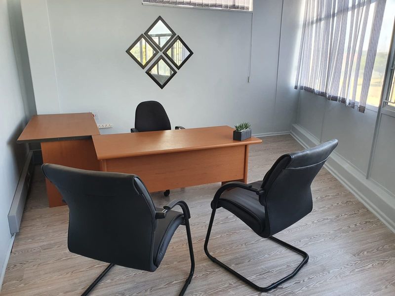 A functional office space featuring light wood-look laminate flooring, large windows with vertical blinds, and neutral wall finishes.