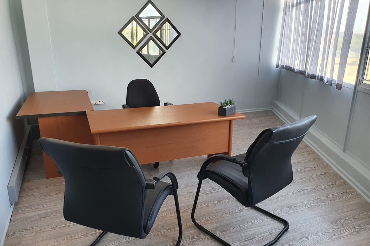 A functional office space featuring light wood-look laminate flooring, large windows with vertical blinds, and neutral wall finishes.