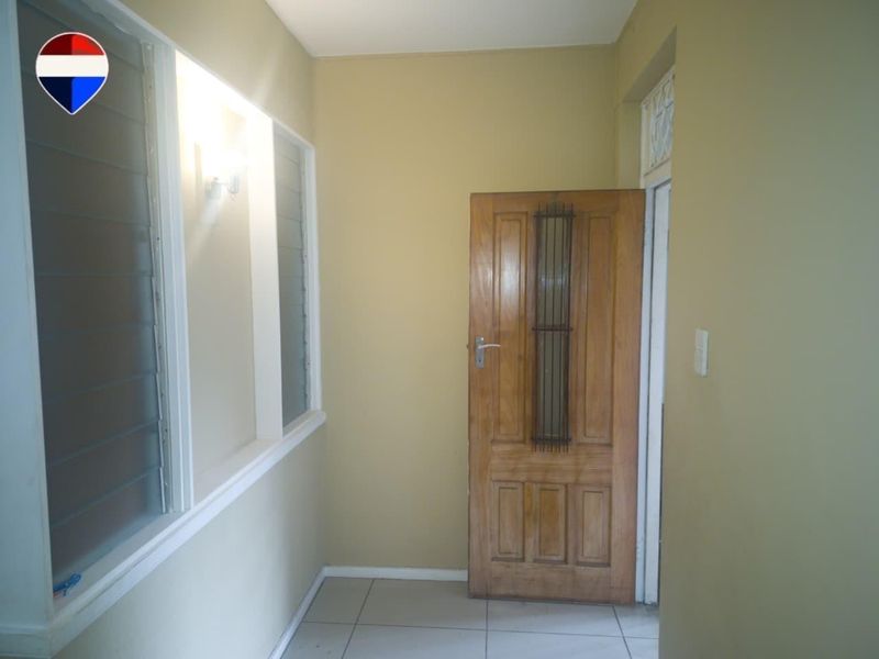 A clean and simple entrance area featuring tiled flooring, a solid timber panel door, and louver windows providing natural light.