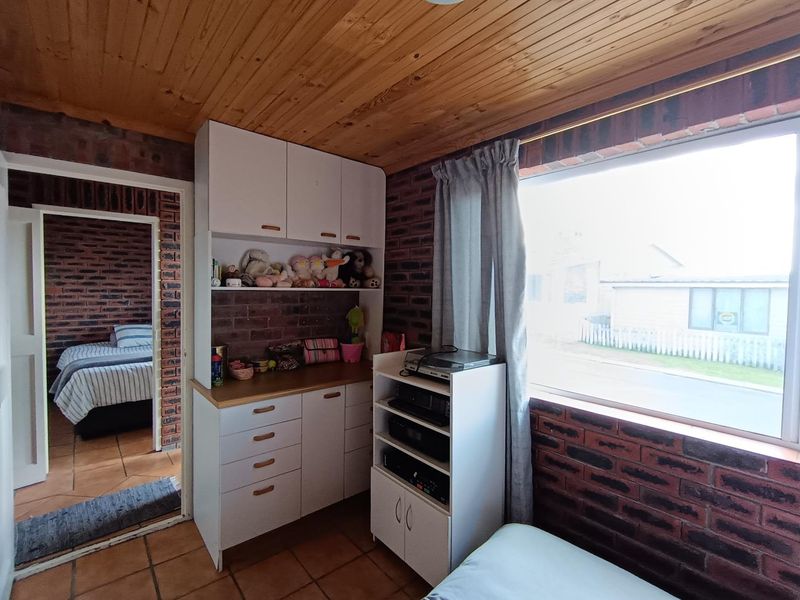 A bedroom featuring exposed brick walls, a timber ceiling, tiled flooring, and built-in cabinetry, offering a rustic aesthetic with potential for modern updates.