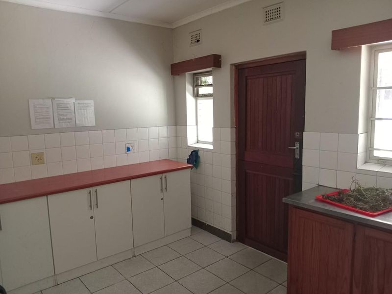A functional kitchen area featuring tiled flooring, built-in cabinetry with laminate countertops, and a timber exterior door with natural light access.