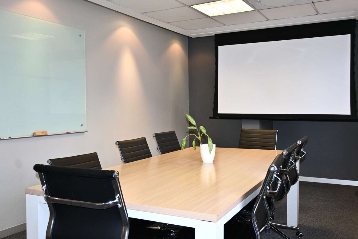 A professional office meeting room featuring a large conference table, wall-mounted glass whiteboard, and a retractable projector screen for presentations.