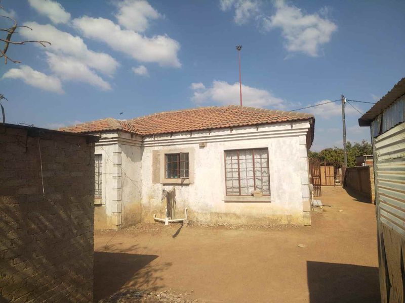 Rear view of a detached house featuring a terracotta tiled roof and steel-framed windows, set on a large plot with a perimeter boundary wall.
