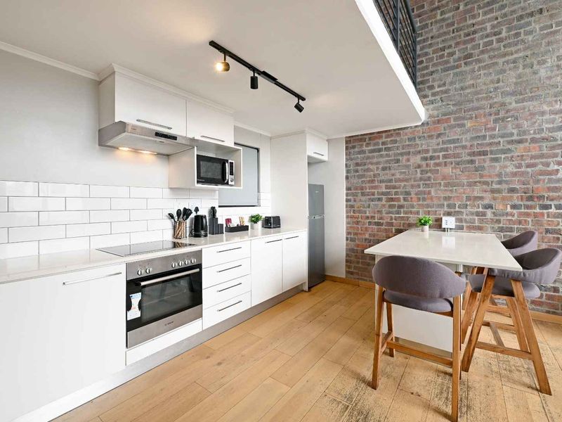 Modern kitchen featuring white cabinetry, subway tile backsplash, built-in appliances, and an exposed brick feature wall, complemented by warm hardwood flooring.