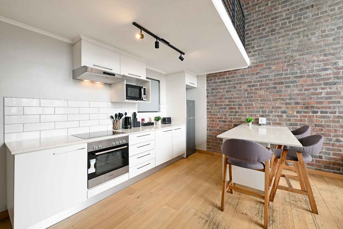Modern kitchen featuring white cabinetry, subway tile backsplash, built-in appliances, and an exposed brick feature wall, complemented by warm hardwood flooring.