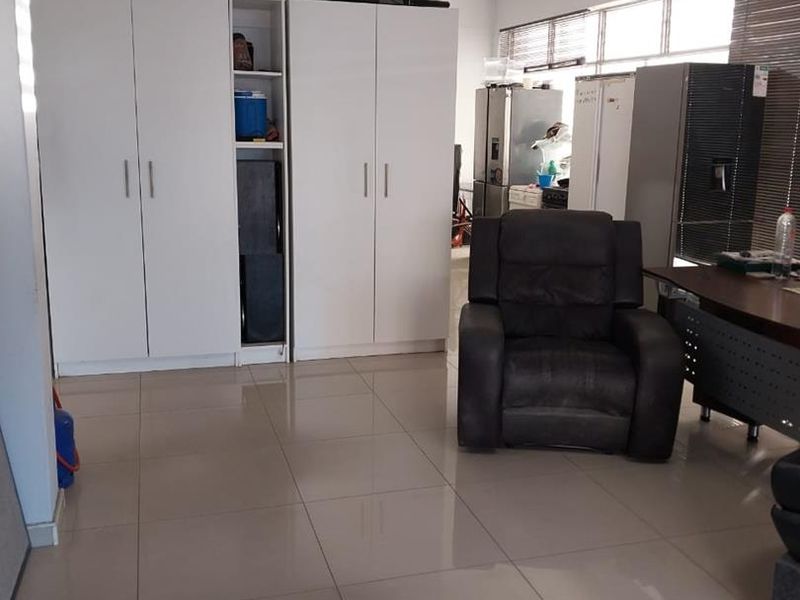 A functional office space featuring tiled flooring, built-in storage cupboards, and large windows with venetian blinds, providing a practical workspace environment.