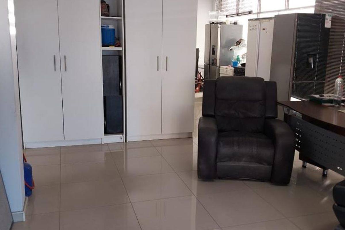 A functional office space featuring tiled flooring, built-in storage cupboards, and large windows with venetian blinds, providing a practical workspace environment.