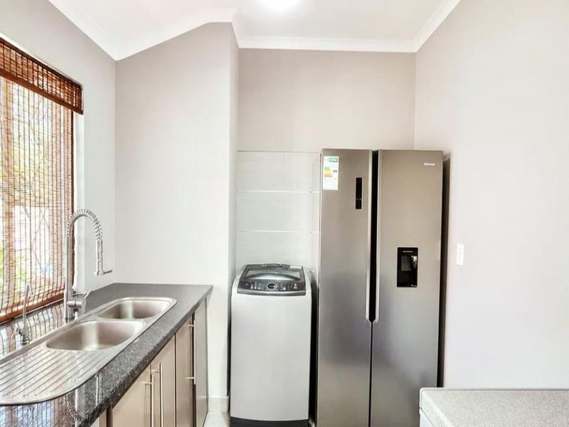 A functional laundry area featuring a double bowl stainless steel sink, granite countertops, and built-in cabinetry with space for appliances.