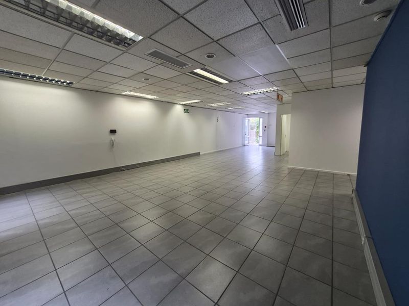 A spacious, vacant office area featuring a suspended ceiling with recessed lighting and neutral tiled flooring, offering a clean and functional workspace.