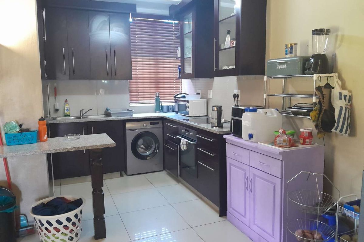 Functional kitchen featuring dark wood cabinetry, granite countertops, built-in oven, and integrated washing machine with tiled flooring and venetian blinds.