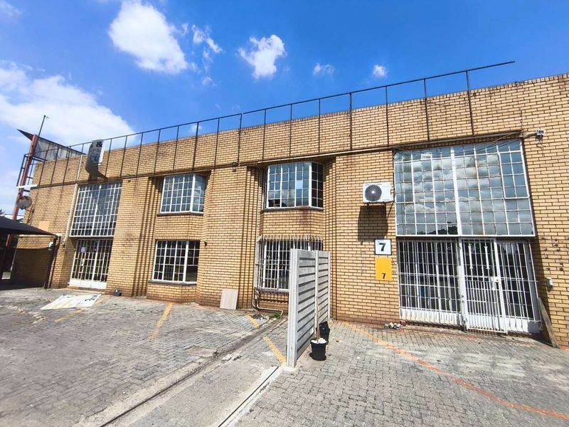 Front elevation of an industrial property featuring face brick construction, steel-framed windows with security bars, and a paved forecourt area.