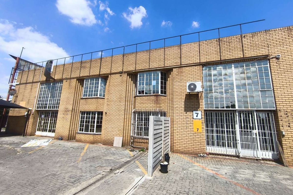 Front elevation of an industrial property featuring face brick construction, steel-framed windows with security bars, and a paved forecourt area.