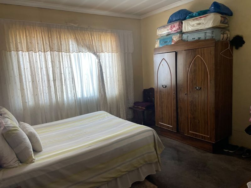 A bedroom featuring a window with curtain rails and standard ceiling cornice, requiring cosmetic updates to the wall finishes and flooring.