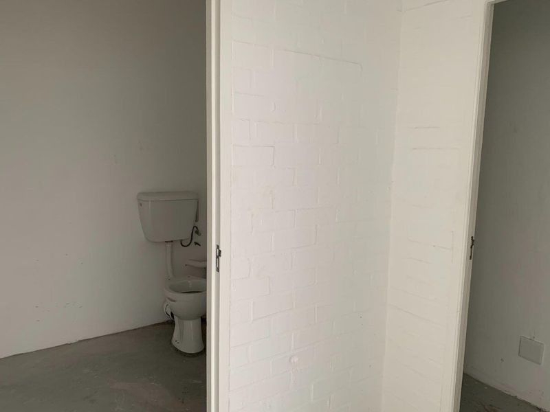A basic, unfinished bathroom space featuring a standard toilet, white painted brick walls, and an exposed concrete floor.