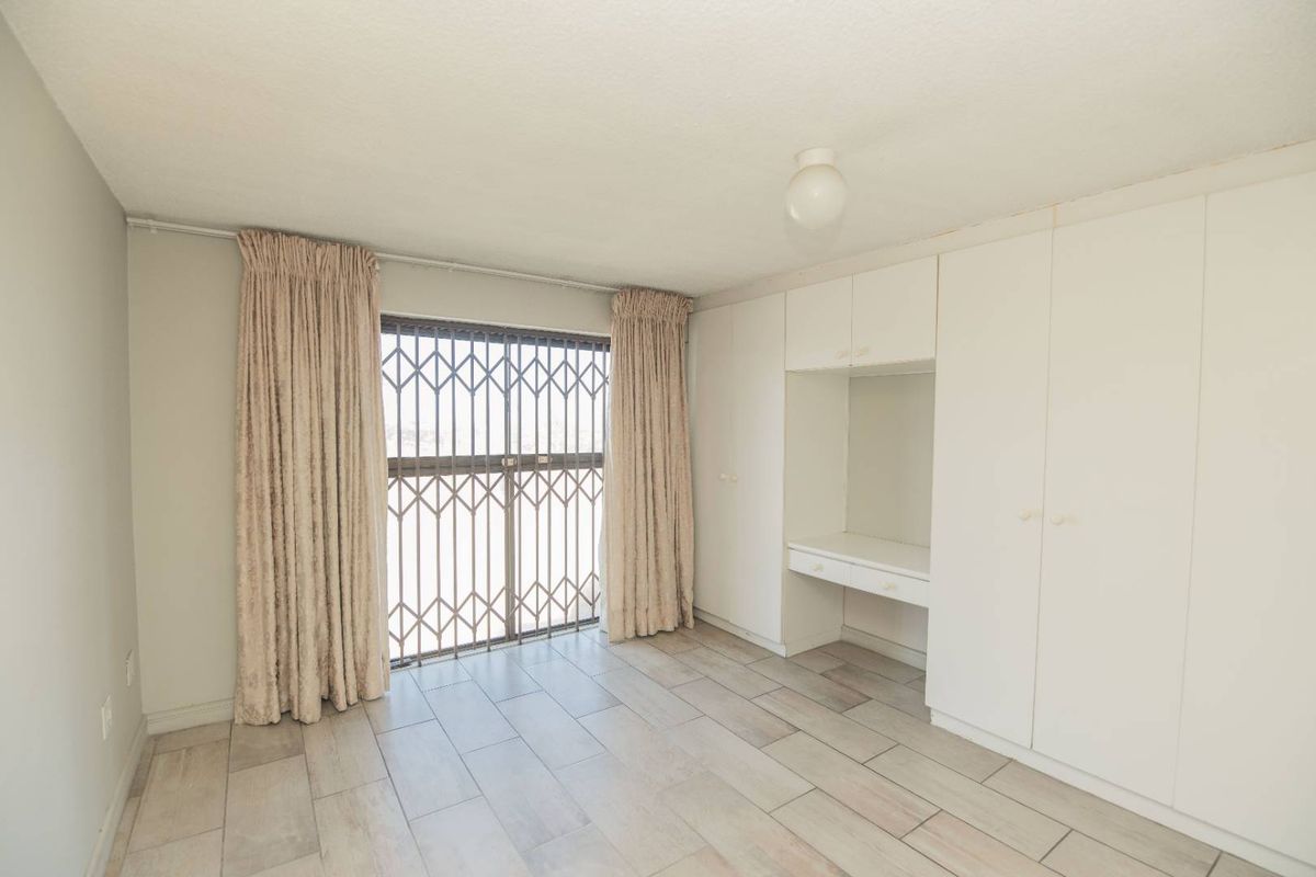 A bright bedroom featuring tiled flooring, built-in storage cupboards with an integrated desk, and a security gate over the window.