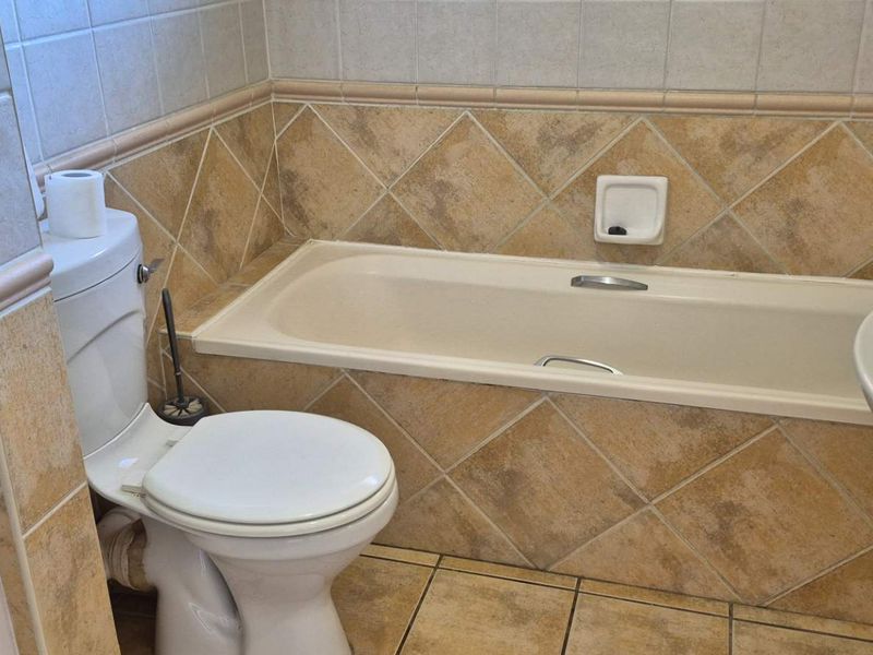 A functional bathroom featuring a built-in bathtub, pedestal sink, and toilet, finished with neutral ceramic wall and floor tiling.