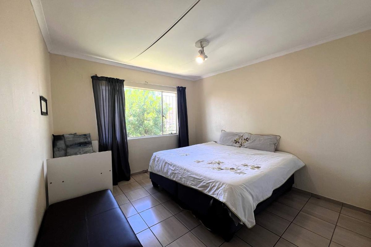 A functional bedroom featuring tiled flooring, a large window for natural light, and a standard ceiling finish.