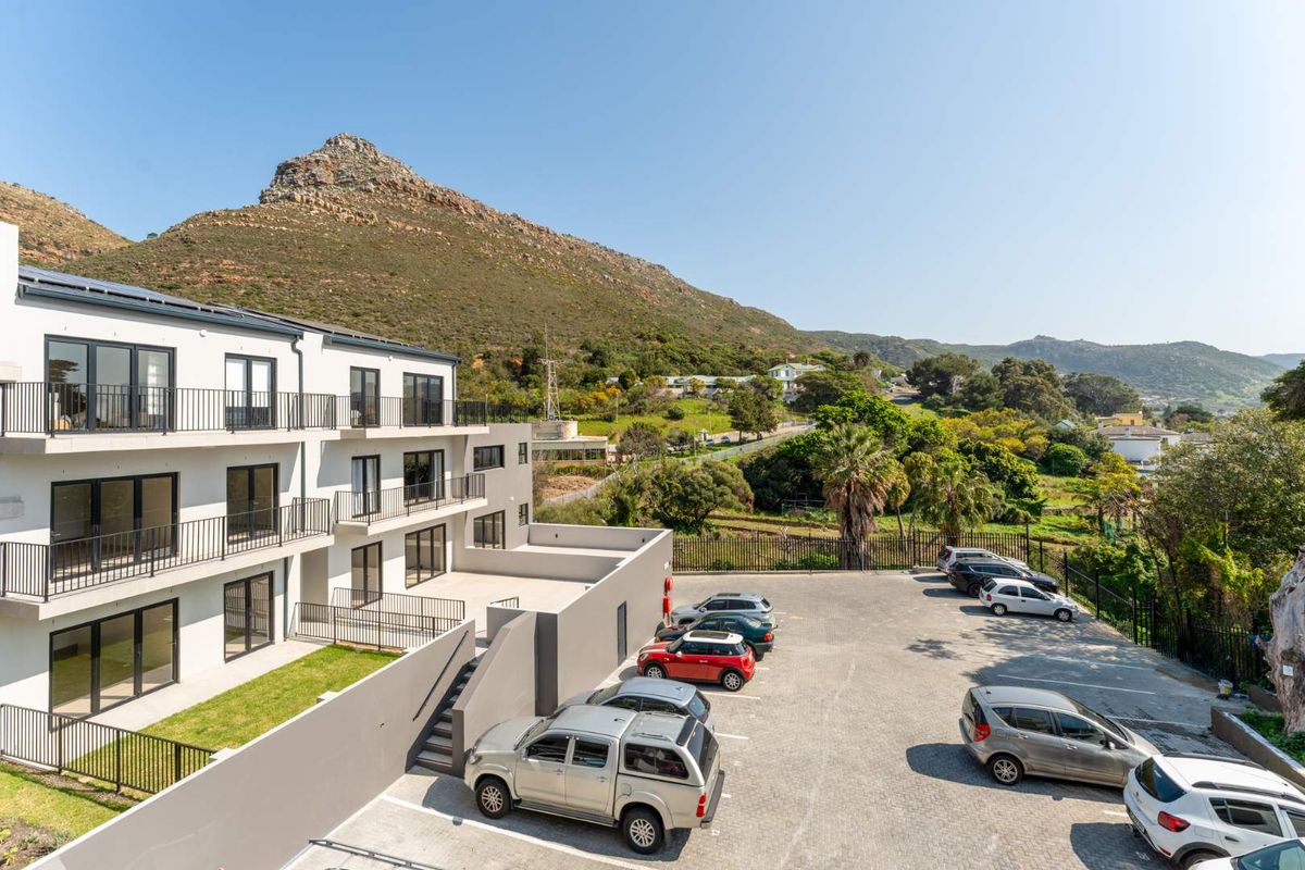 Exterior view of a modern apartment complex featuring balconies, paved parking area, and scenic mountain views.