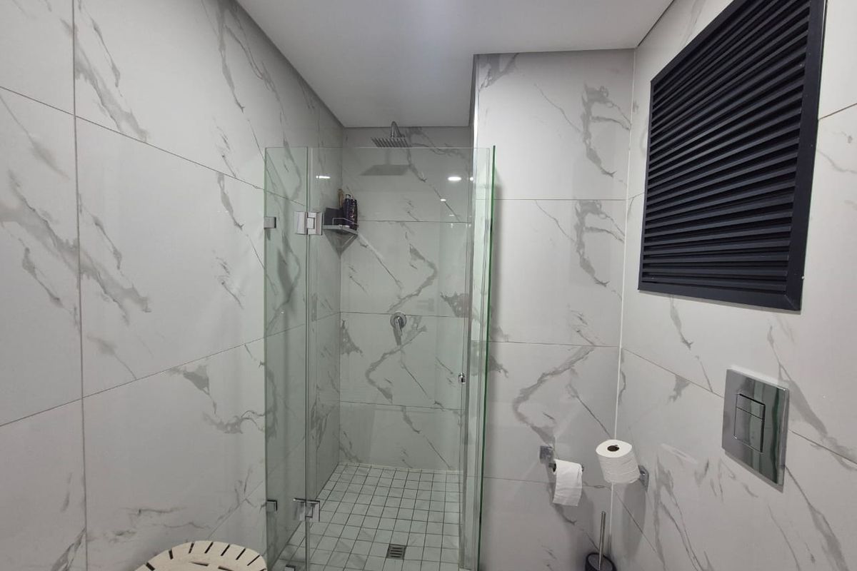 Modern bathroom featuring a glass-enclosed shower with a rain shower head, finished with elegant marble-look wall tiles and contemporary fixtures.
