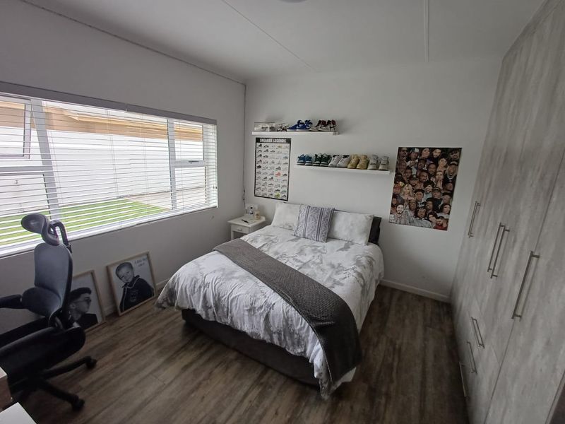A well-maintained bedroom featuring modern laminate flooring, a large built-in wardrobe, and a wide window providing natural light.