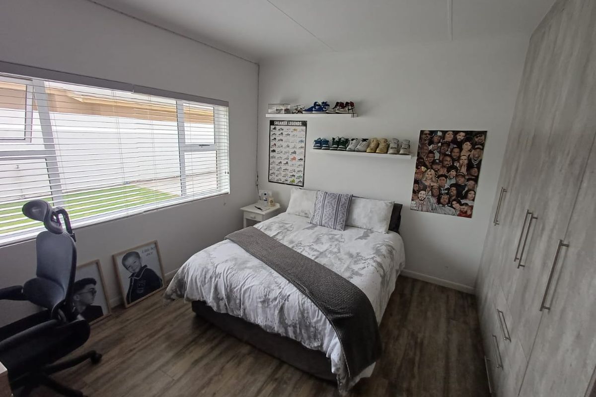 A well-maintained bedroom featuring modern laminate flooring, a large built-in wardrobe, and a wide window providing natural light.
