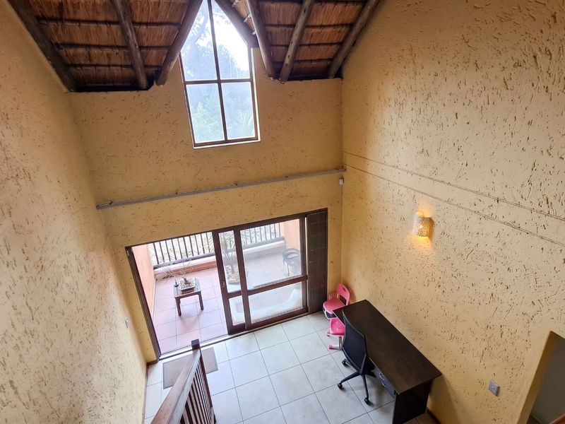 Double-volume living area featuring a high thatched ceiling with exposed rafters, textured walls, tiled floors, and direct access to a private balcony.