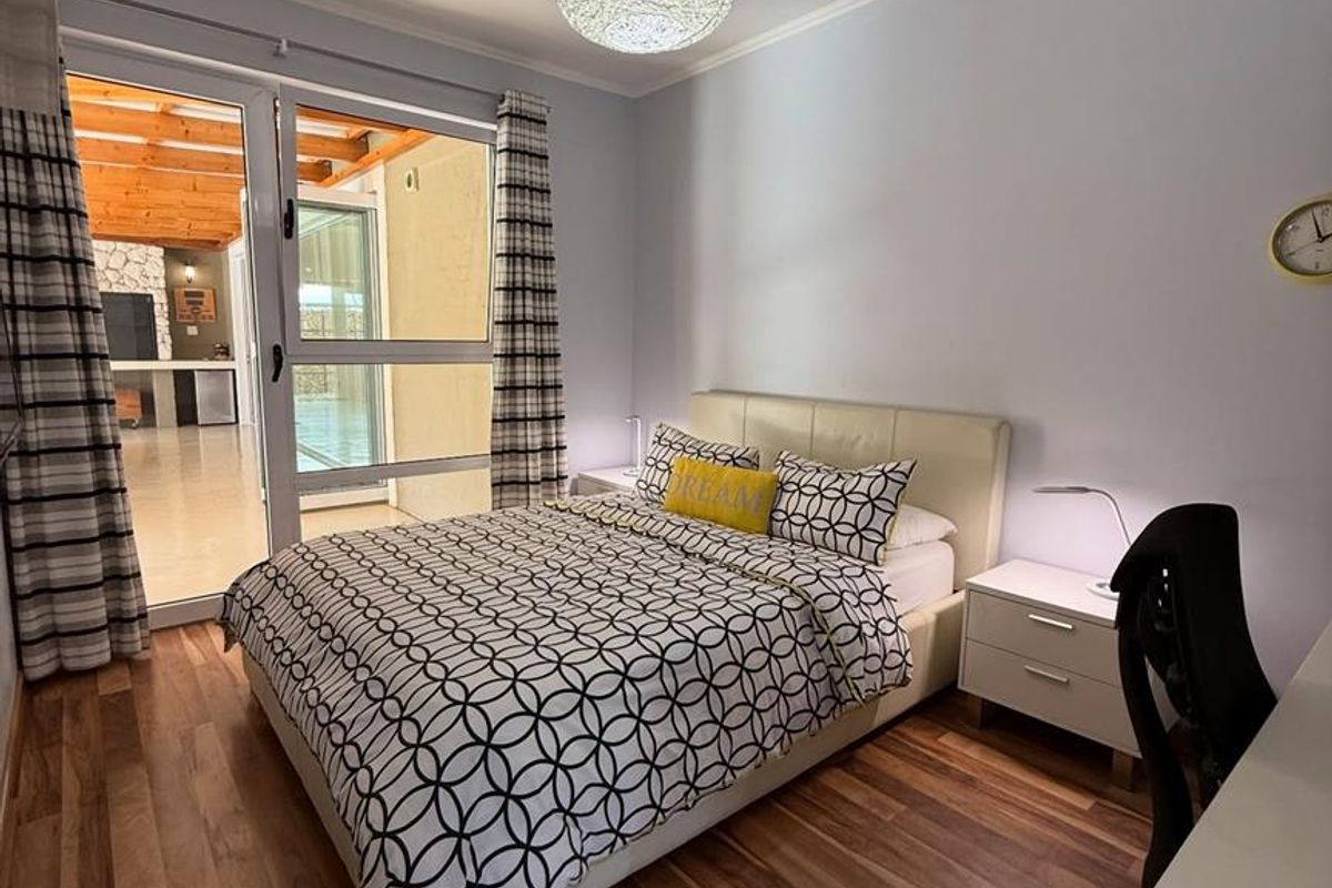 A well-maintained bedroom featuring wood-look flooring, a modern pendant light, and large glass sliding doors providing direct access to an outdoor patio area.