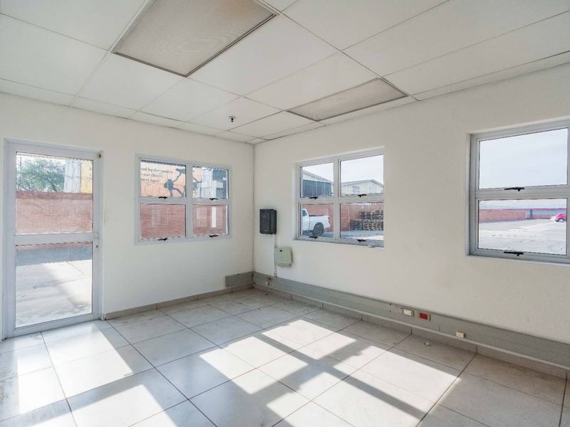 A vacant, functional office space featuring tiled flooring, a suspended ceiling, and multiple windows providing natural light, suitable for various industrial or commercial uses.