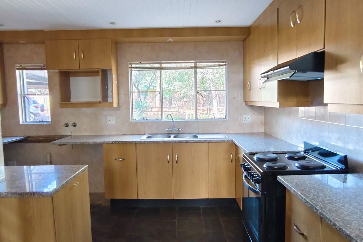 A functional kitchen featuring wood-veneer cabinetry, granite-look countertops, a double-basin sink, and a built-in extractor fan with a freestanding stove.