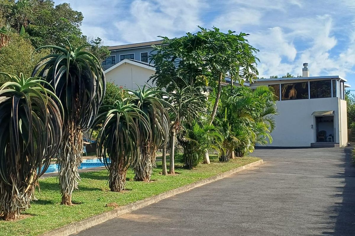 A view of the property exterior featuring a paved driveway, landscaped garden with mature aloe plants, and a glimpse of the swimming pool area.