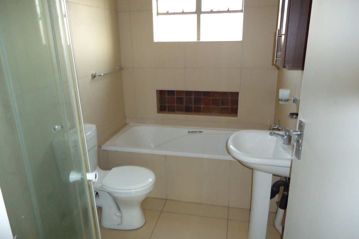 A functional bathroom featuring a bathtub, pedestal sink, toilet, and a separate shower enclosure with neutral wall and floor tiling.
