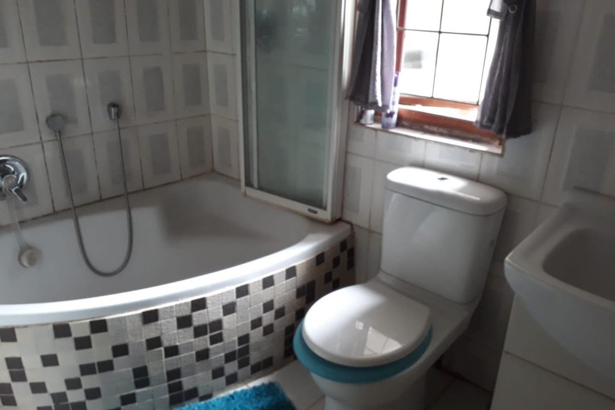 A compact bathroom featuring a built-in bathtub with mosaic tile detailing, a standard toilet, and a washbasin, requiring some cosmetic updates.
