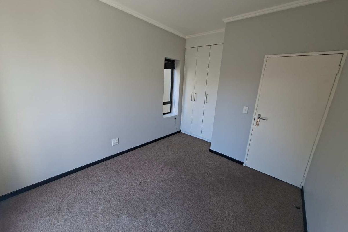 An empty bedroom featuring neutral walls, built-in cupboards, and carpeted flooring, providing a blank canvas for personalization.