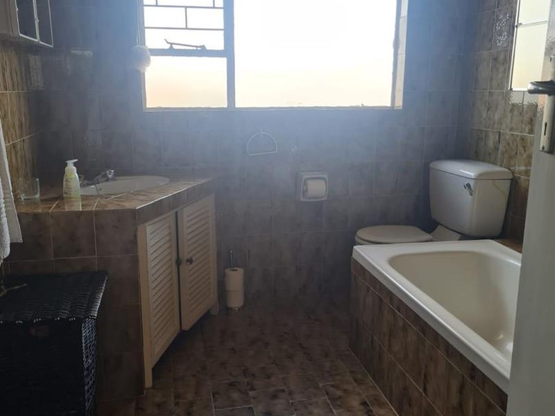 A functional bathroom featuring a built-in vanity, bathtub, and toilet, finished with dated brown ceramic tiling throughout.