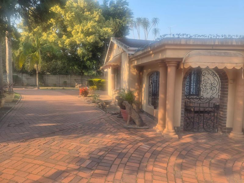 Front exterior view of a house featuring a paved driveway, decorative columns, and a secure gated entrance with an awning.