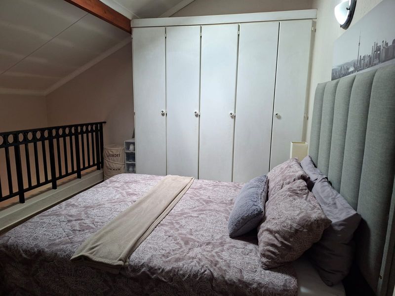 A cozy bedroom featuring a vaulted ceiling with an exposed timber beam, built-in wardrobe storage, and a mezzanine-style railing overlooking the lower level.