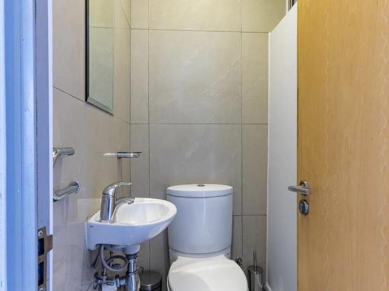 A compact, modern guest bathroom featuring neutral wall tiles, a wall-mounted basin, and a standard toilet.