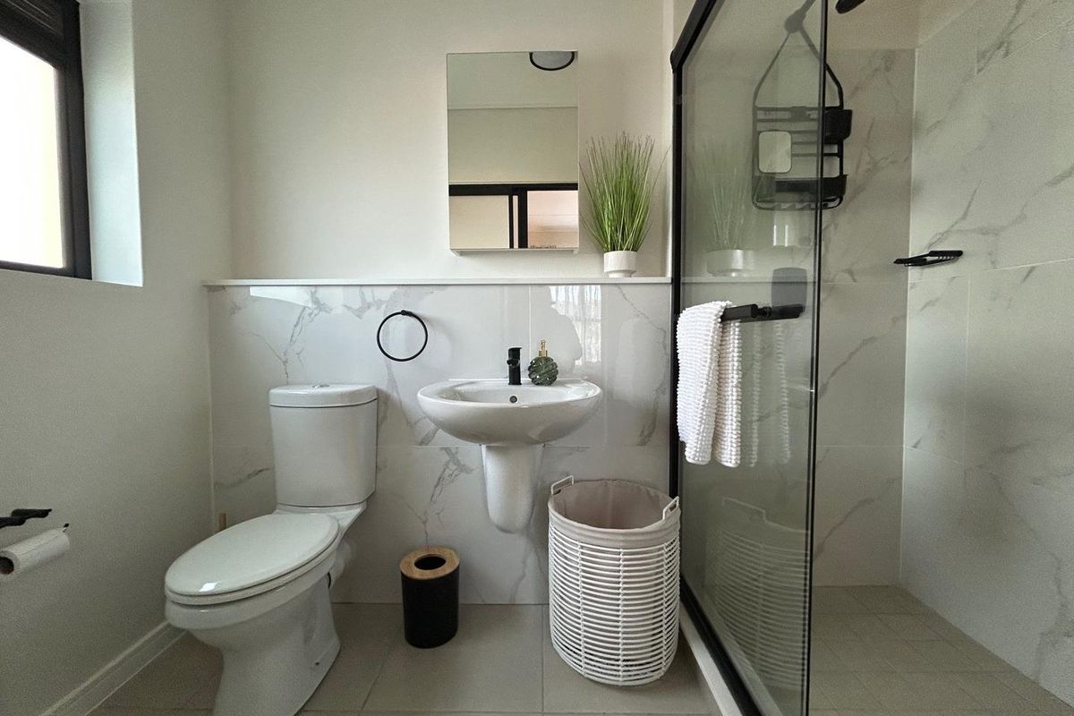 Modern bathroom featuring a glass-enclosed shower, pedestal sink, and toilet with marble-look wall tiling and neutral floor tiles.